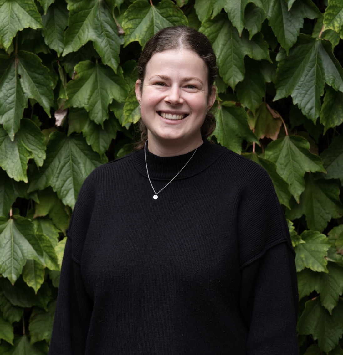A woman in a black sweater standing in front of an ivy covered wall.