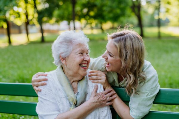 A woman and an elderly woman are sitting on a bench in a park, enjoying their quality time together as family.