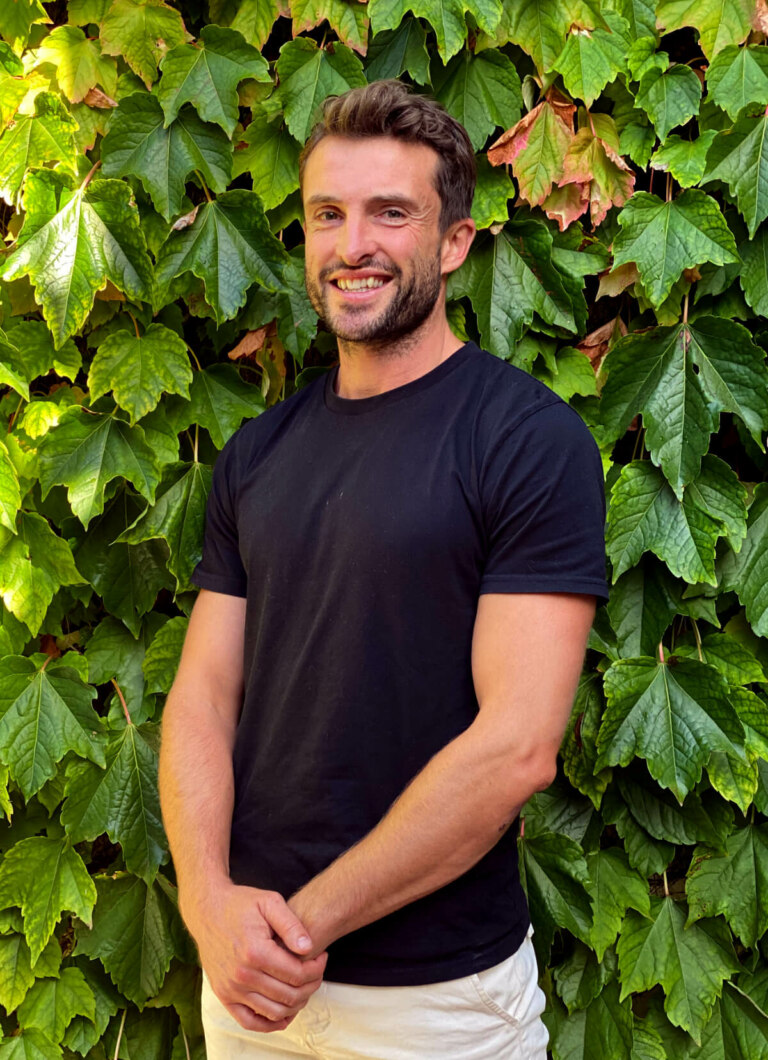 A man in a black shirt named Chris Jellis standing in front of an ivy covered wall.