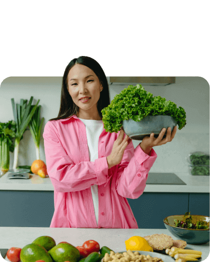 A woman holding a bowl of vegetables in front of a kitchen.