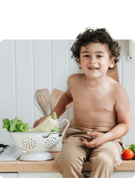 A young nutritionist boy sitting on a kitchen counter with vegetables in a colander.