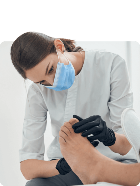 A podiatrist wearing a mask and gloves is examining a patient's foot.