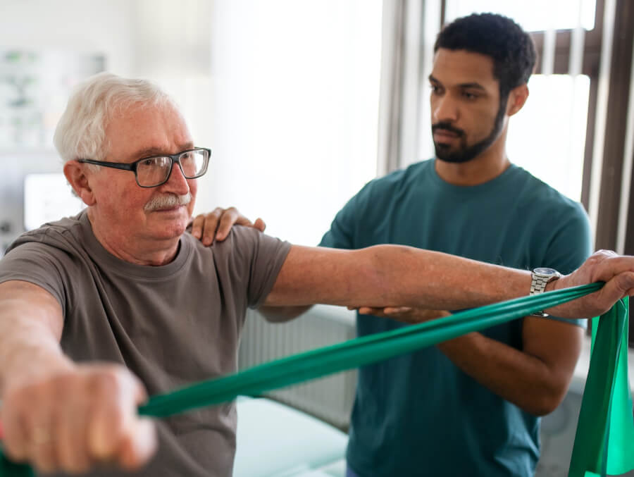 An older man is being helped by a physical therapist.