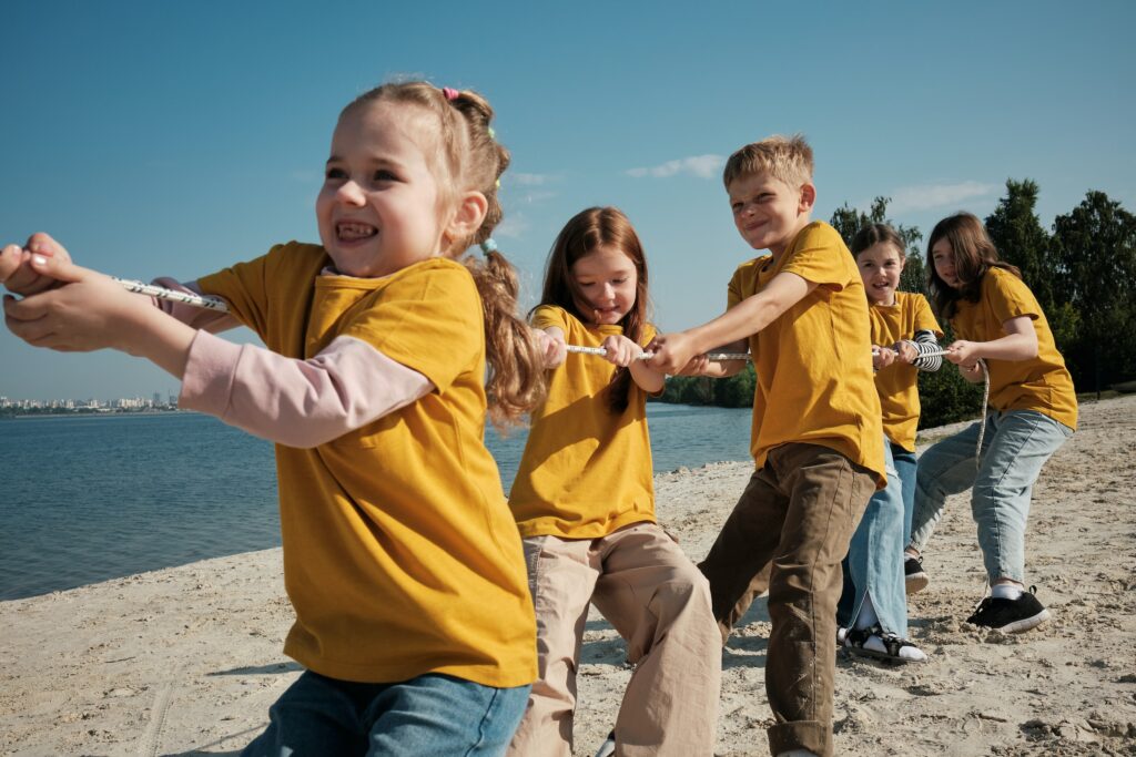 Expect a group of kids engaging in motor milestones as they play tug of war on the beach.