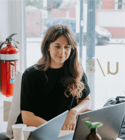 A woman working at a table in Prahran with two laptops.