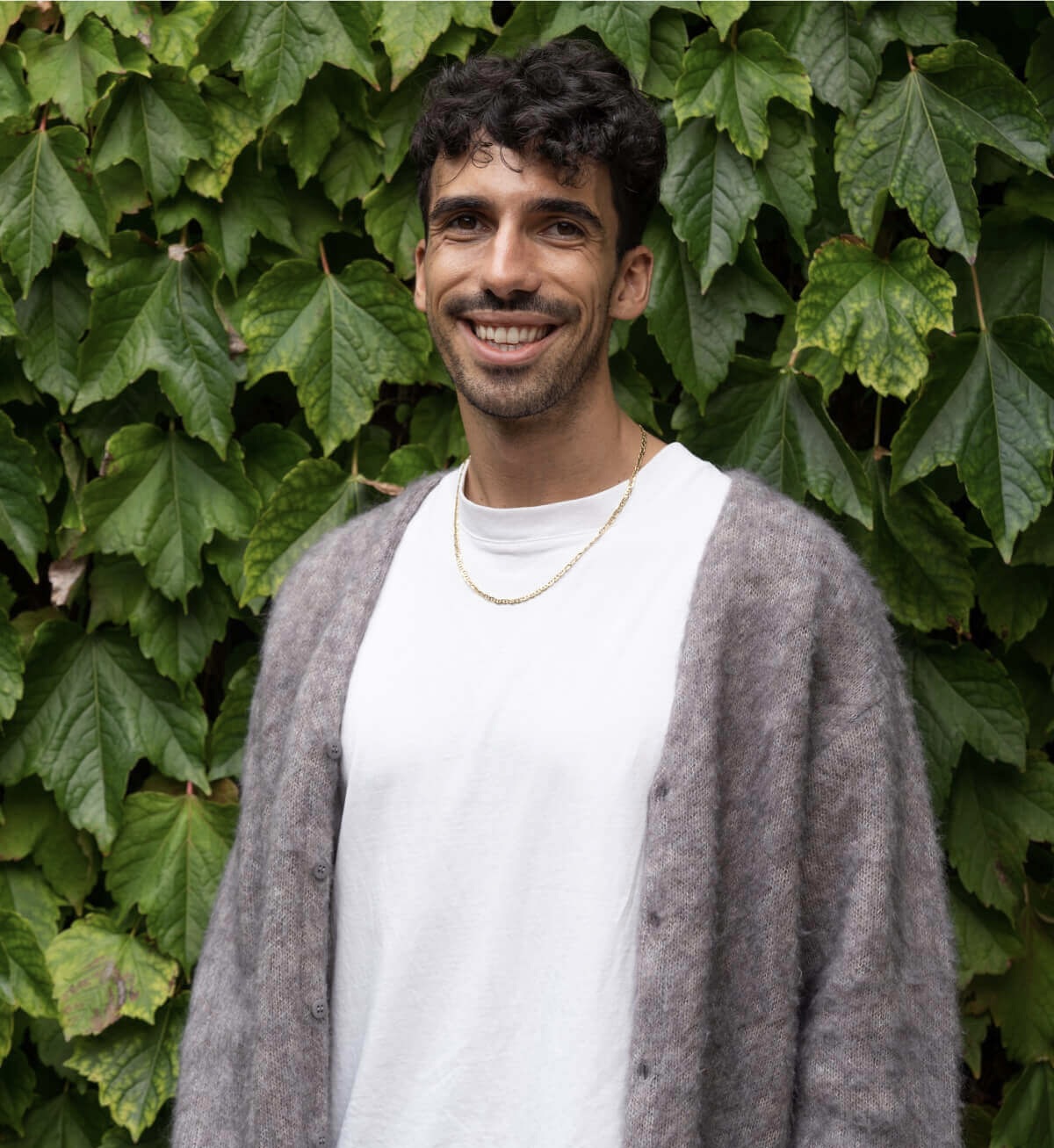 A man smiling in front of an ivy covered wall.