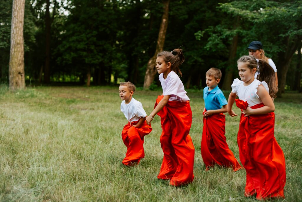 A group of children engaged in play, running and engaging their social skills in red skirts on the grass.